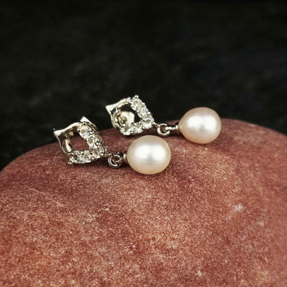 Witte zoetwater parel oorbellen met stras steentjes liggend op rode steen | Bling Pearl Heart W