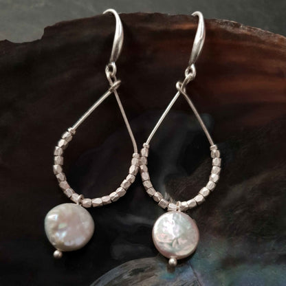 Lange witte zoetwater parel oorbellen met witte coin parel en mat zilver hangend in schelp | Milany Silver