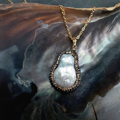 Detail van zoetwater parelketting met witte parelhanger met gouden en zwarte stras steentjes en goud edelstaal liggend in schelp | Bright Minimal Gold Teardrop