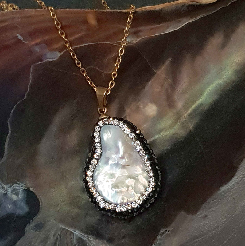 Detail van zoetwater parelketting met witte parelhanger met zilveren en zwarte stras steentjes en goud edelstaal liggend in schelp, vooraanzicht | Bright Minimal Gold Teardrop