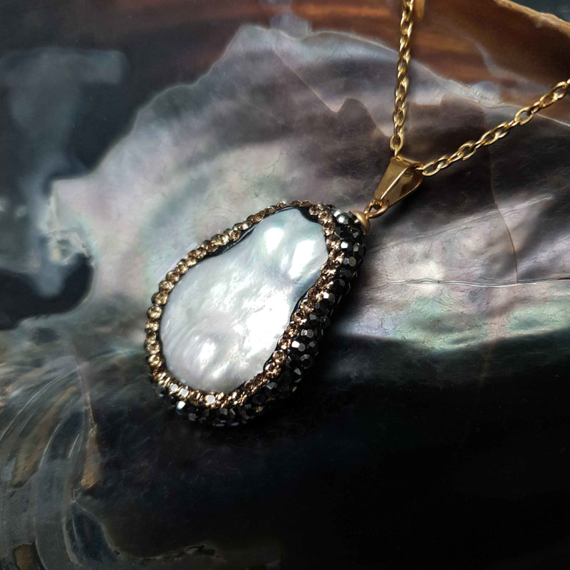 Detail van zoetwater parelketting met witte parelhanger met gouden en zwarte stras steentjes en goud edelstaal liggend in schelp, zijaanzicht | Bright Minimal Gold Teardrop