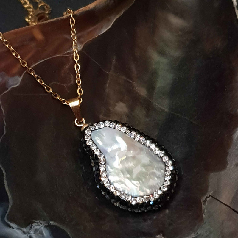 Detail van zoetwater parelketting met witte parelhanger met zilveren en zwarte stras steentjes en goud edelstaal liggend in schelp | Bright Minimal Gold Teardrop