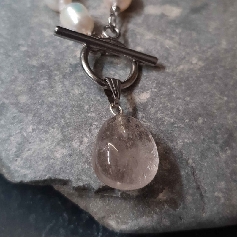 Detail van handgeknoopte zoetwater parelketting met witte parels, zilver edelstaal en rook kwarts hanger liggend op steen | Toggle Pearl Smokey Quartz