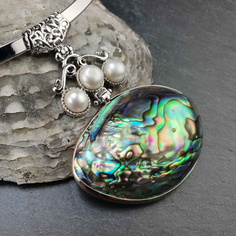 Detail van zoetwater parelketting met witte parels en abalone hanger aan zilveren spang liggend tegen schelp | Three Pearl Abalone