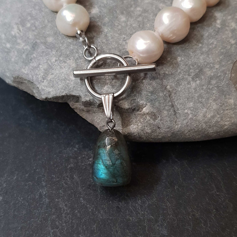 Detail van witte zoetwater parelketting met labradoriet hanger en zilver edelstaal liggend tegen kei | Toggle Big Pearl Labradorite