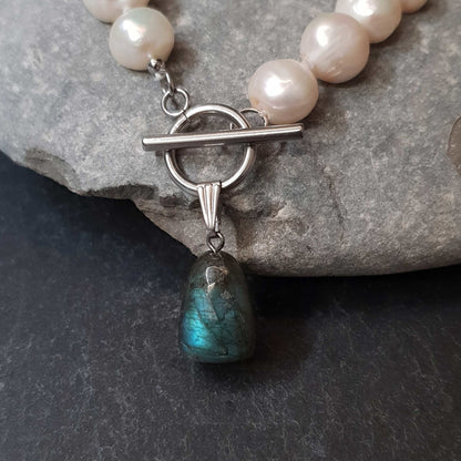 Detail van witte zoetwater parelketting met labradoriet hanger en zilver edelstaal liggend tegen kei | Toggle Big Pearl Labradorite