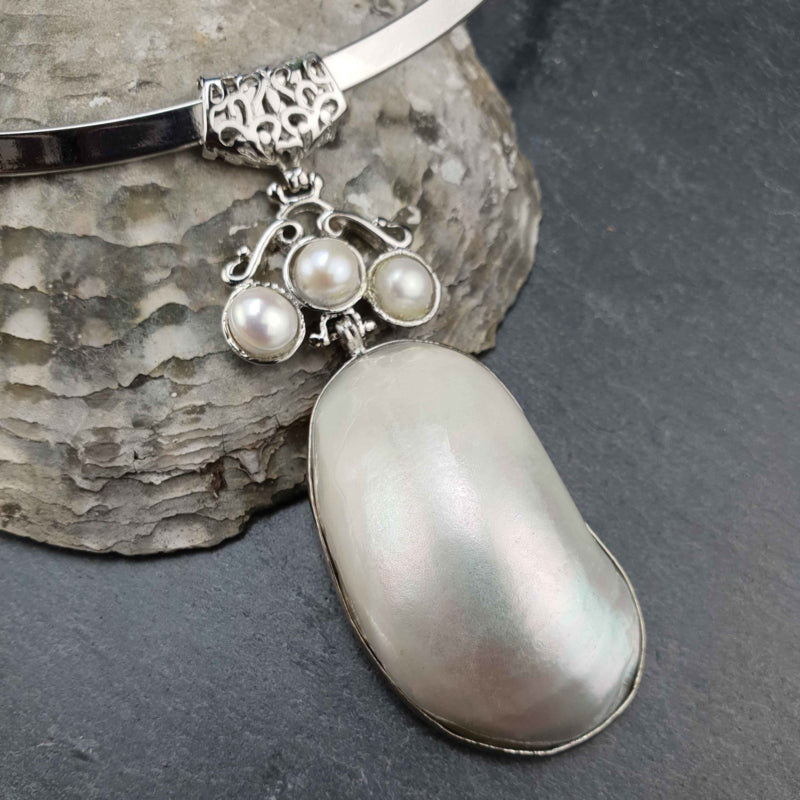 Detail van korte zoetwater parel ketting met witte parels en witte parelmoer schelp hanger aan spang liggend tegen schelp | Three Pearl Shell Long