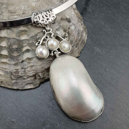 Detail van korte zoetwater parel ketting met witte parels en witte parelmoer schelp hanger aan spang liggend tegen schelp | Three Pearl Shell Long