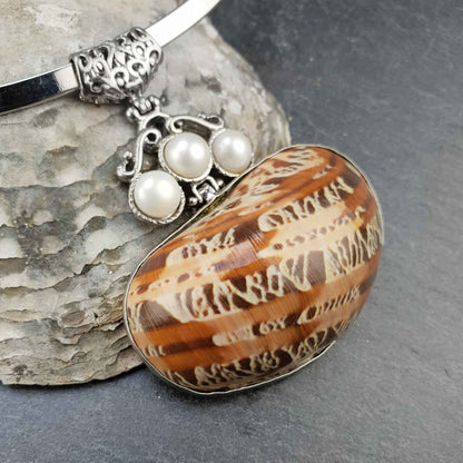 Detail van korte zoetwater parel ketting met witte parels en een bruine schelp Hanger aan spang liggend tegen schelp | Three Pearl Brown Shell