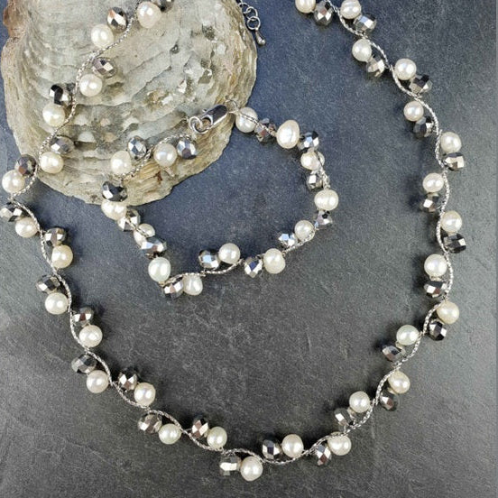 Zoetwater parel set bestaande uit een parelketting en parel armband met witte parels en zilver facet geslepen glaskristallen liggend tegen schelp | set Silana