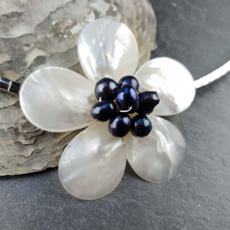 Detail van zoetwater parelketting met zwart blauwe parels, witte parelmoer in bloem vorm en zilver edelstaal liggend tegen schelp | set Fleury B