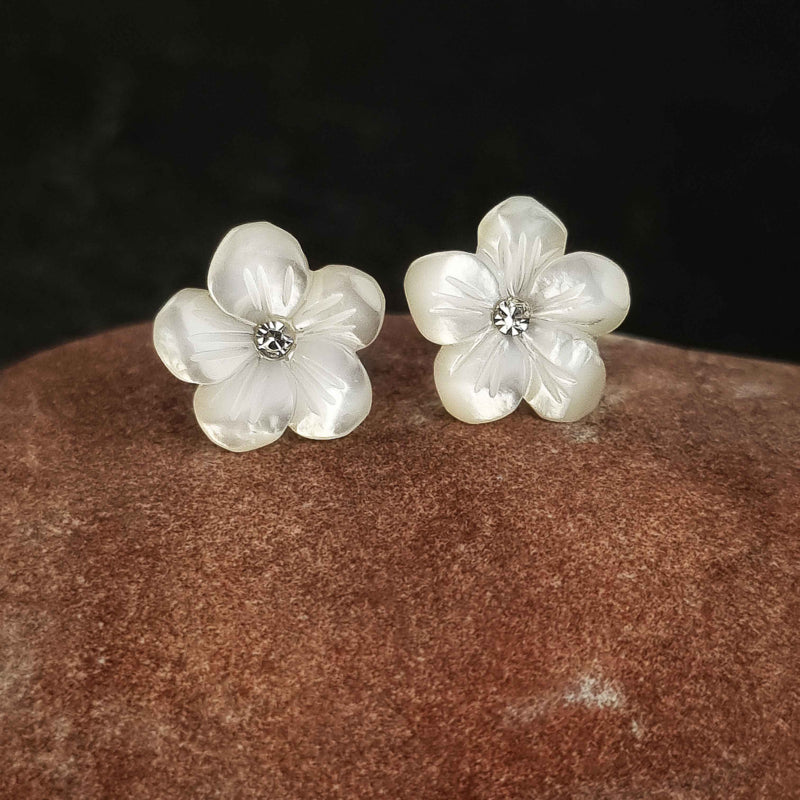 Witte parelmoeren oorknopjes met bloem en stras steentje liggend op rode steen | Big Flower Bling
