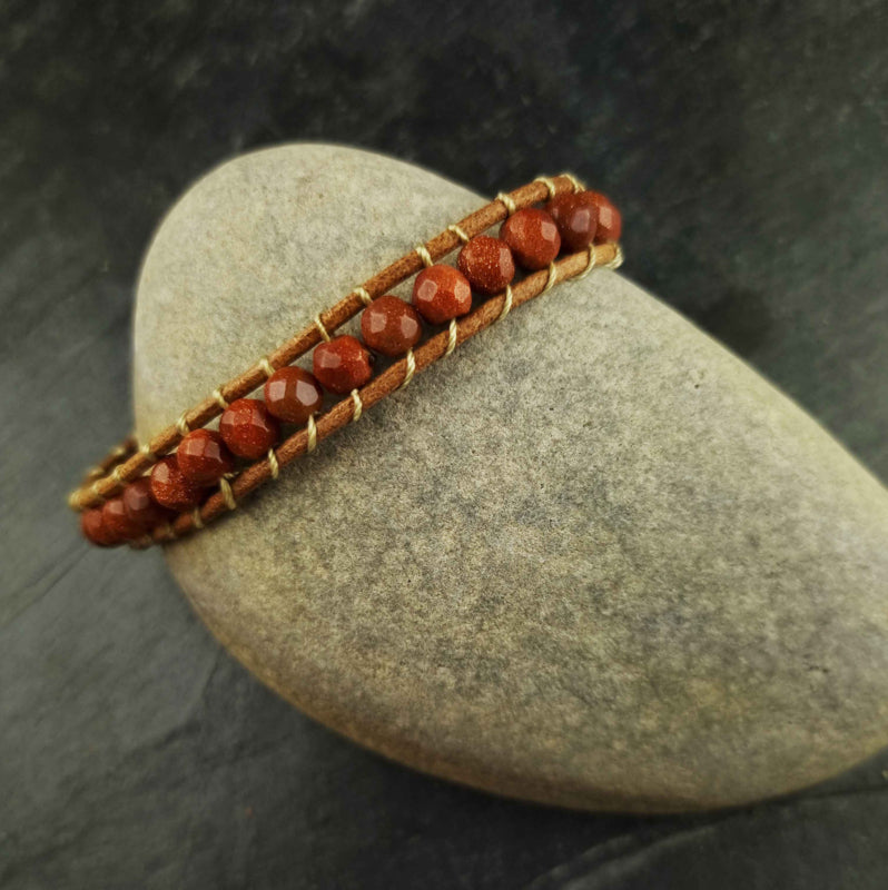 Bruin edelstenen armband met goudvuur / goudsteen en leer liggend op kei | Wrap Gold Sand