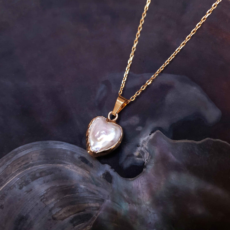 Detail van zoetwater parelketting met witte parel hanger in hart vorm en goud edelstaal liggend in schelp | Golden Heart White Pearl