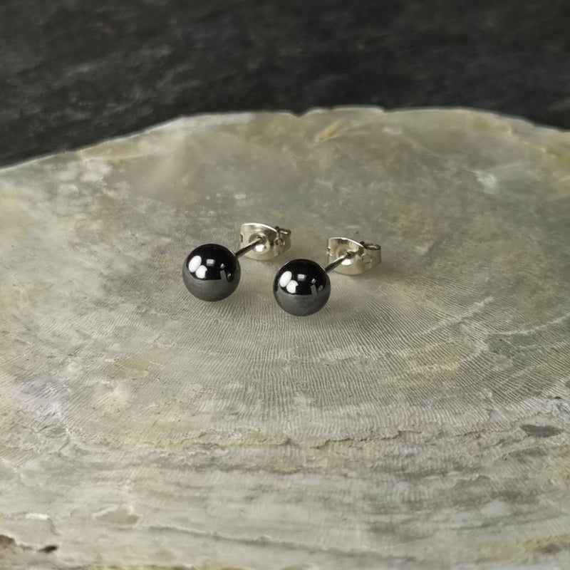 Zwarte edelstenen oorbellen met hematiet stenen liggend op witte schelp, zwarte hematiet oorknopjes 6 mm liggend op witte schelp