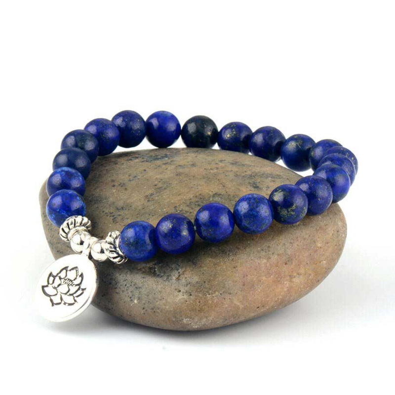 Lapis lazuli armband met zilver lotus bedeltje, elastisch blauw edelstenen armband liggend op steen