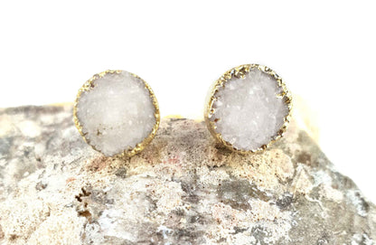 Witte edelstenen oorbellen met druzy agaat en goud liggend op steen, witte edelstenen oorknopjes