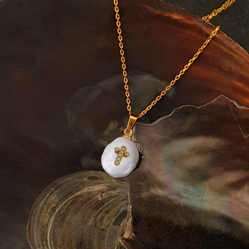 Detail van zoetwater parelketting met witte parel hanger met stras steentjes in kruis motief en goud edelstaal liggend in schelp | Coin Pearl Golden Cross