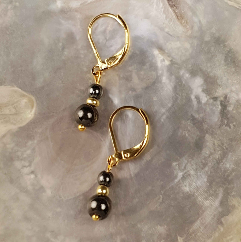 Zwarte edelstenen oorbellen met goud edelstaal liggend op witte schelp | Double Hematite Gold