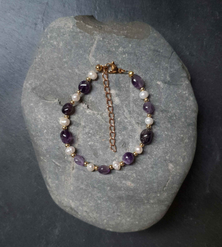 Wit zoetwater parel armband met paarse amethist edelsteen en goud edelstaal liggend op steen