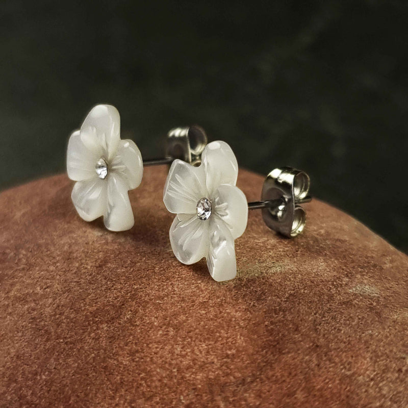 Witte parelmoeren oorknopjes met bloem en stras steentje liggend op rode steen, zijaanzicht | Big Flower Bling