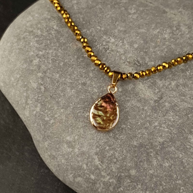 Bruine parelketting met edelstaal en gouden kristallen liggend op grijze steen | set Badia