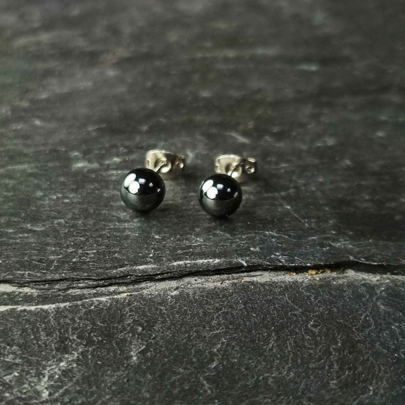 Zwarte edelstenen oorbellen met hematiet stenen liggend op leisteen, zwarte hematiet oorknopjes 6 mm liggend op leisteen