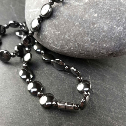 Zwarte edelstenen ketting met magneetslot en hematiet stenen liggend op grijze steen