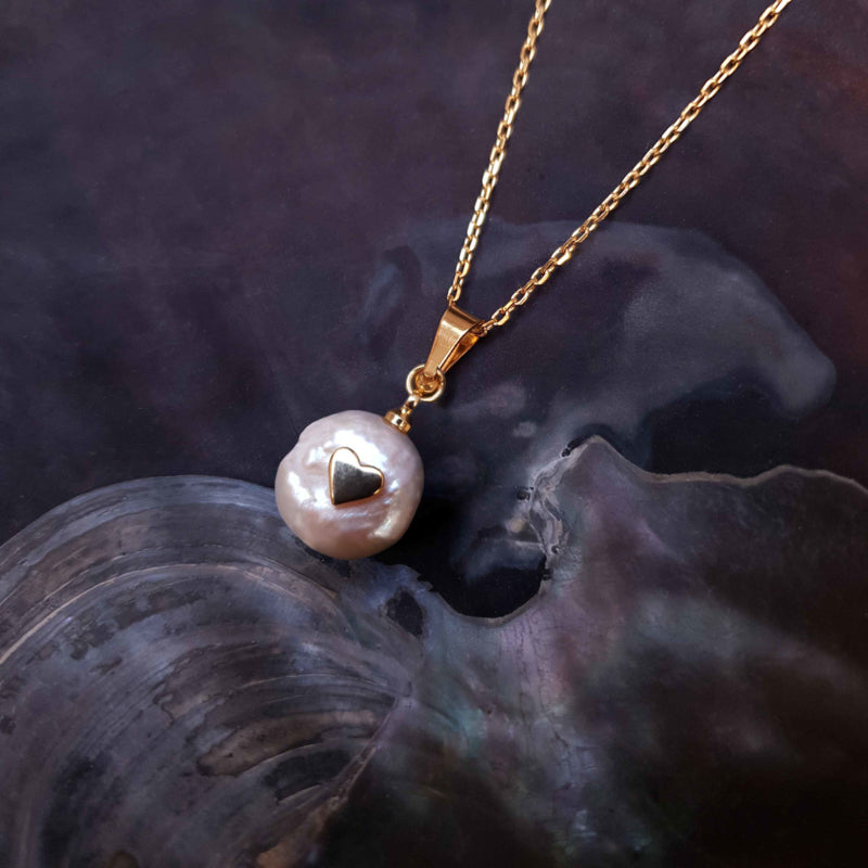 Detail van zoetwater parelketting met witte parel met gouden hartje en goud edelstaal liggend in schelp | Golden Love Pearl