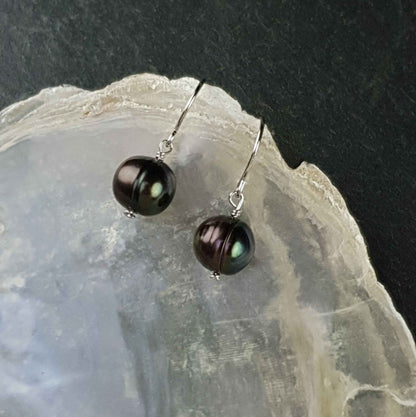 Petroleum kleurige zoetwater parel oorbellen met gerhodineerden zilveren oorbelhaakjes liggend op witte schelp | Peacoin