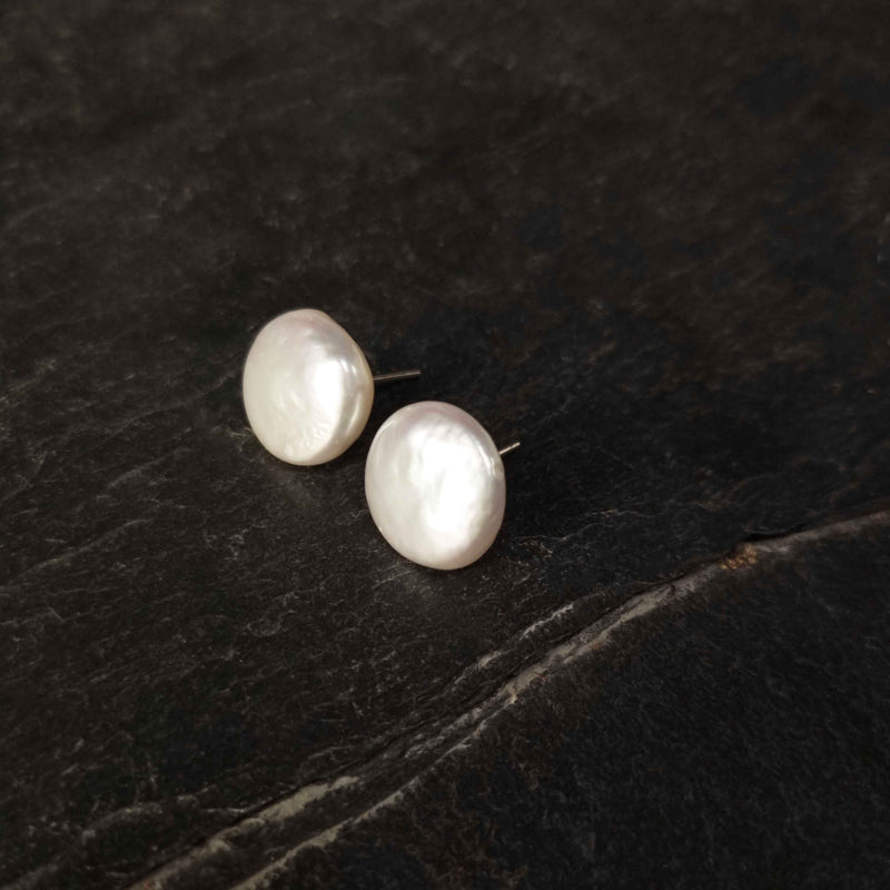 Grote witte zoetwater parel oorbellen met sterling zilveren oorstekers liggend op zwarte leisteen, parel oorknopjes | Big White Coin Pearl