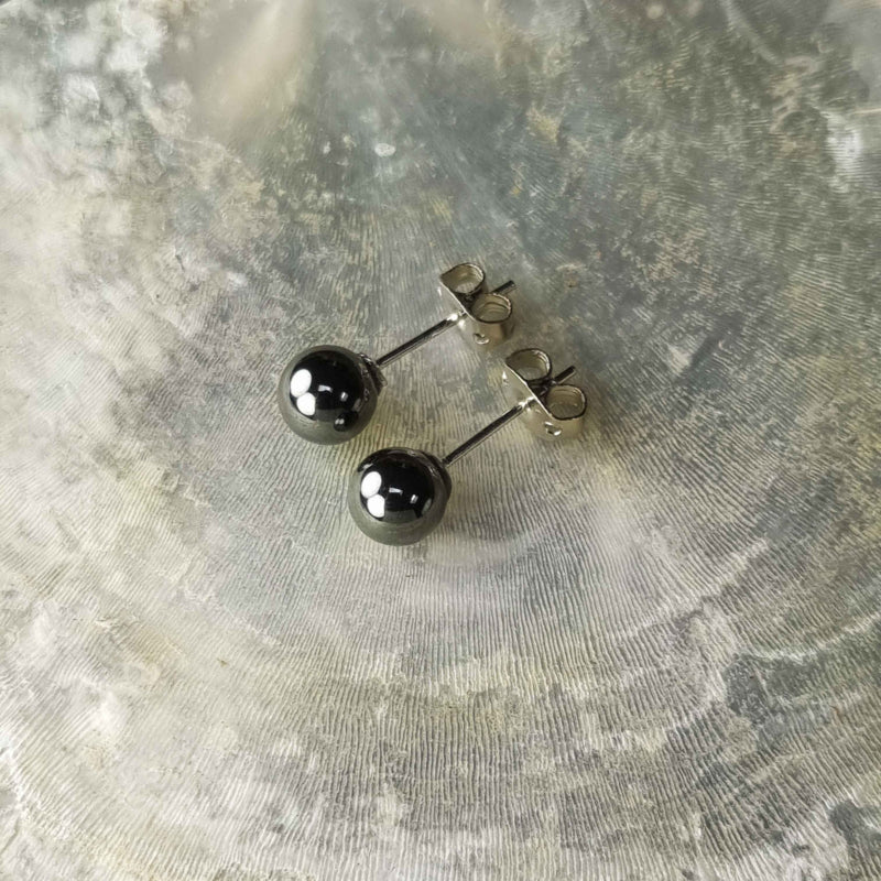 Zwarte edelstenen oorbellen met hematiet stenen, zwarte hematiet oorknopjes 6 mm liggend op witte schelp bovenaanzicht